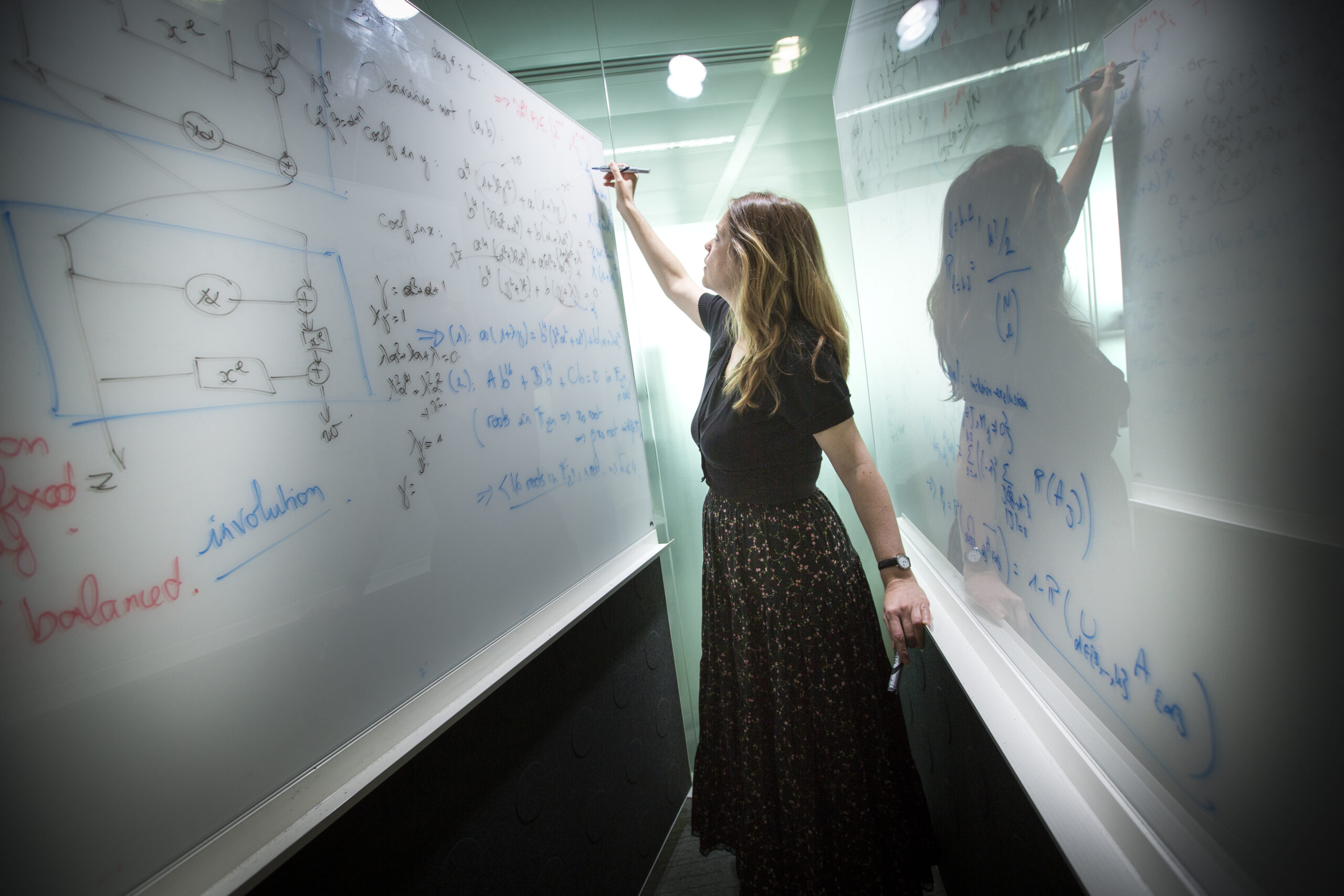 Picture of a woman, standing in between two whiteboards and writing equations on them 