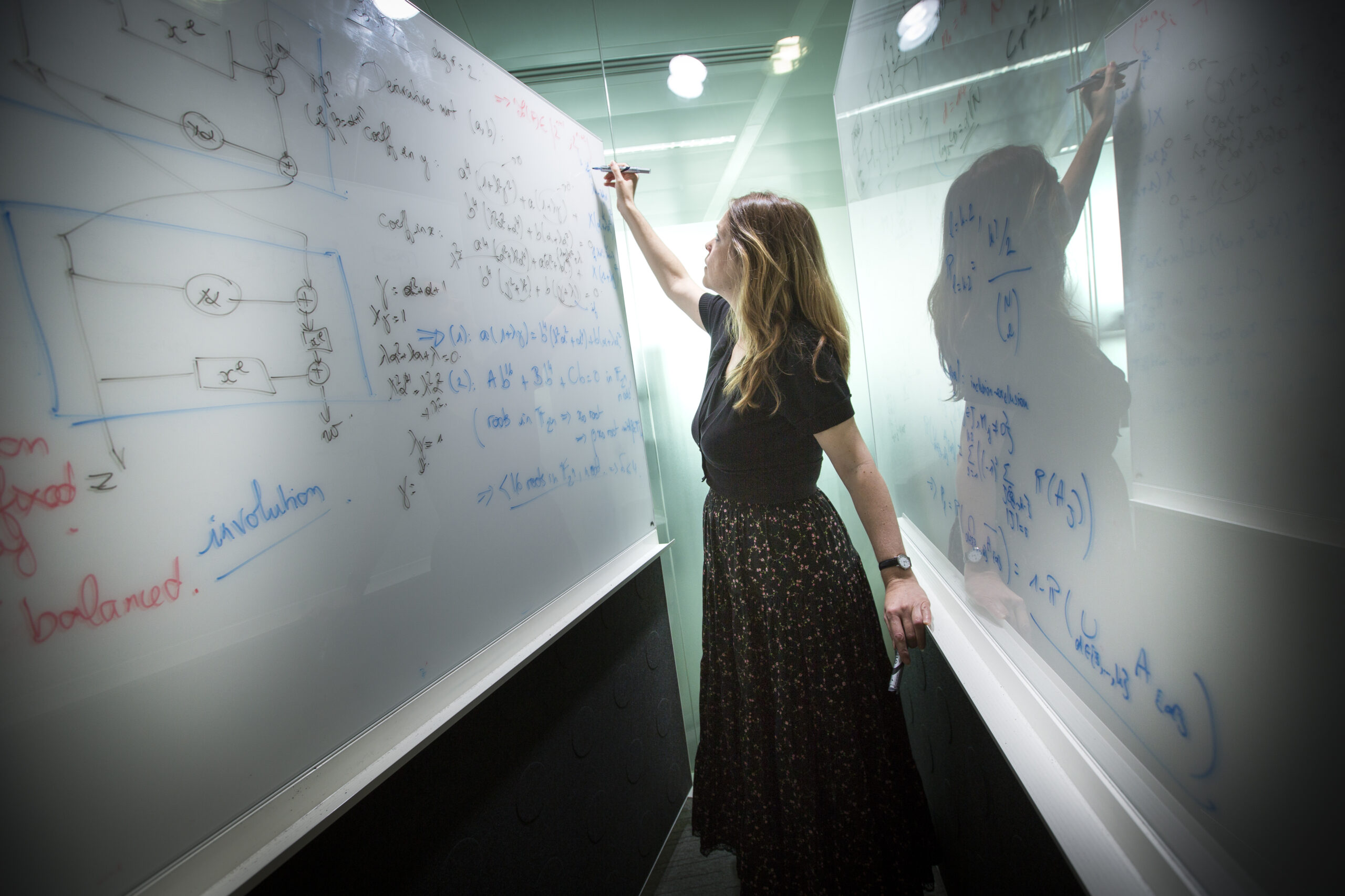 Picture of a woman, standing in between two whiteboards and writing equations on them