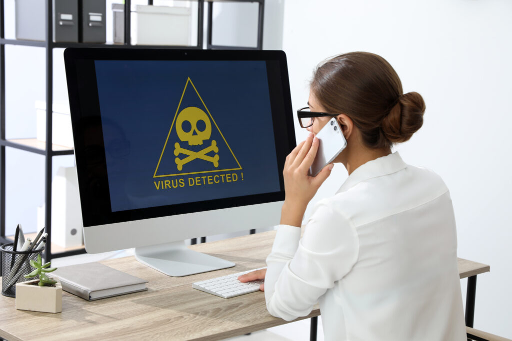 Office worker in front of computer with warning about virus attack on screen