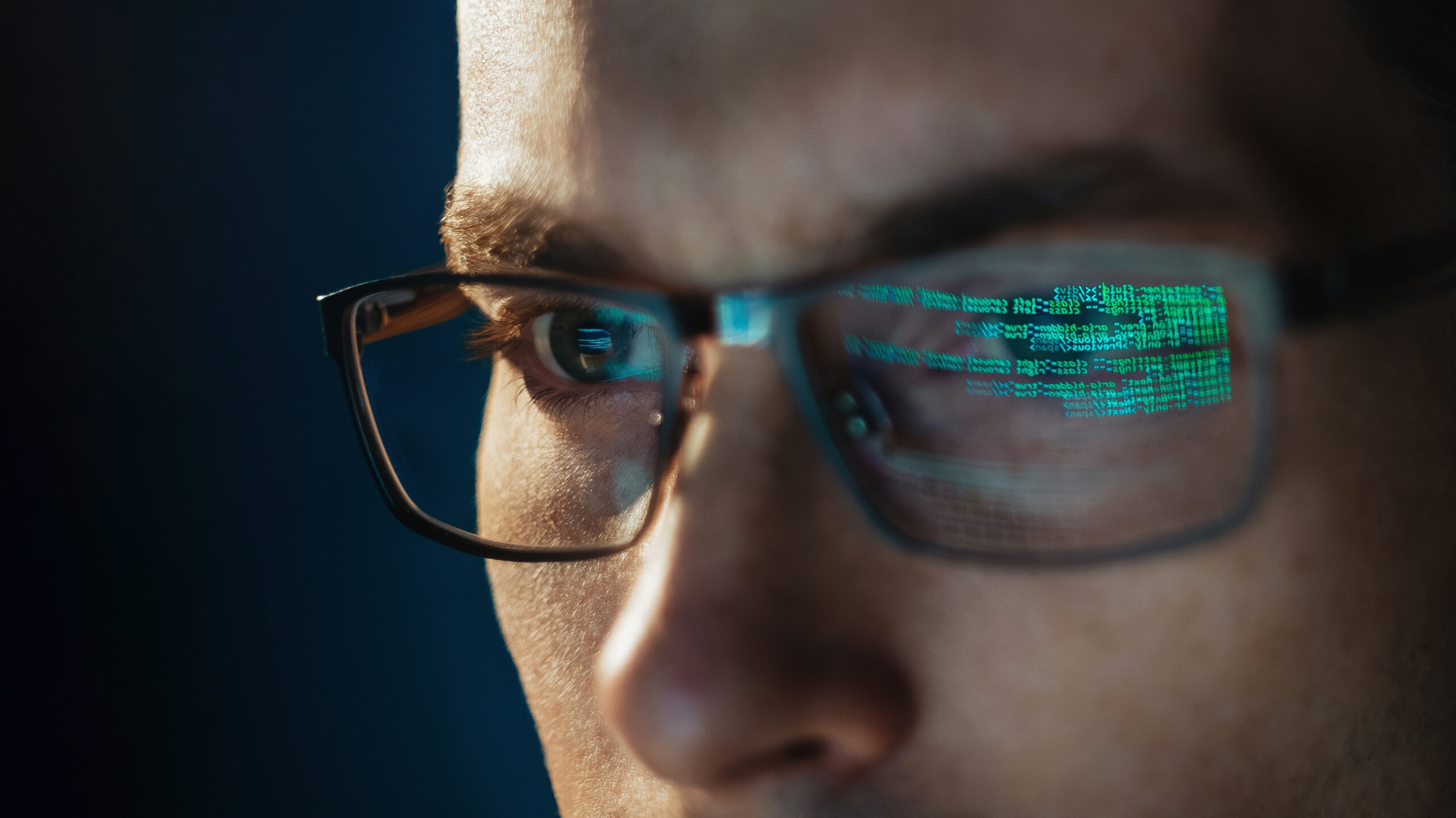 Close-up portrait of focused software engineer wearing eyeglasses looking at computer screen working with big data. 